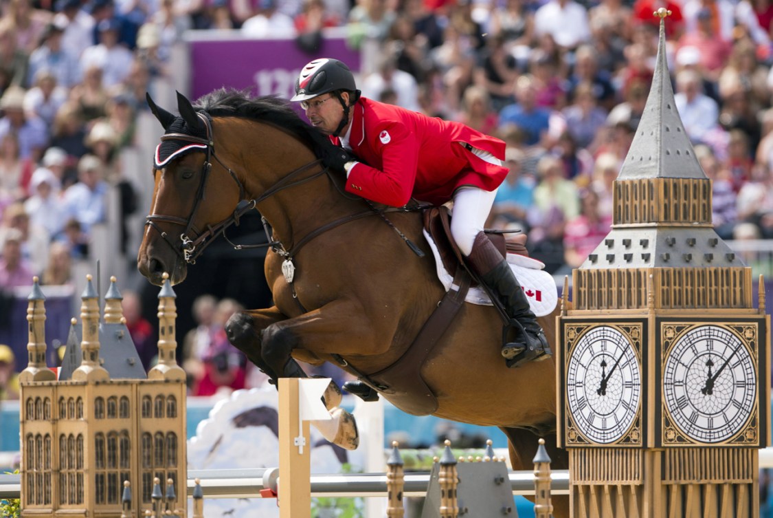 Un cavalier sur un cheval brun franchi un obstacle. 