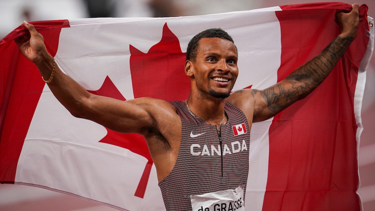 Andre De Grasse tient le drapeau canadien derrière lui.