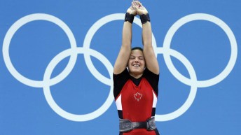 Christine Girard lève les bras dans les airs, les anneaux olympiques à l'arrière plan.