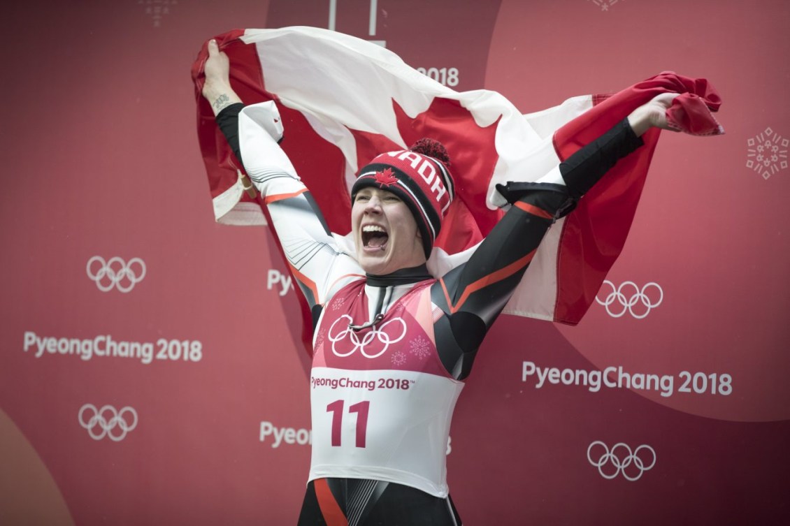 Alex Gough a un énorme sourire et tient le drapeau canadien
