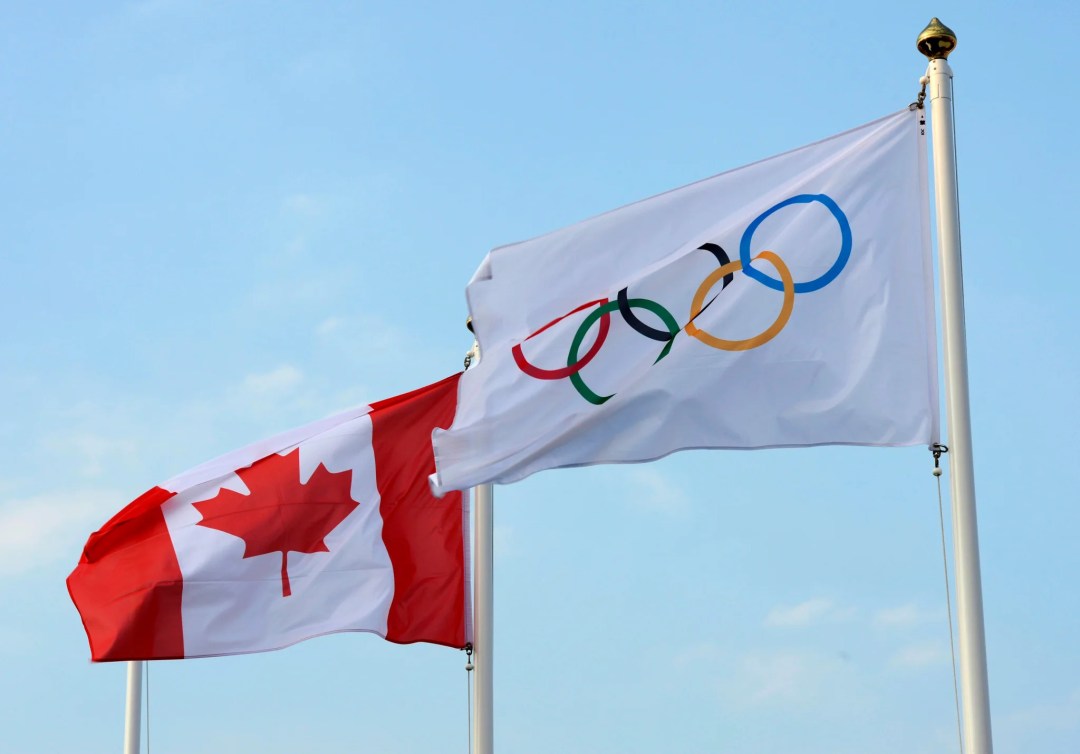 Un drapeau canadien et un drapeau olympique flottent au vent.
