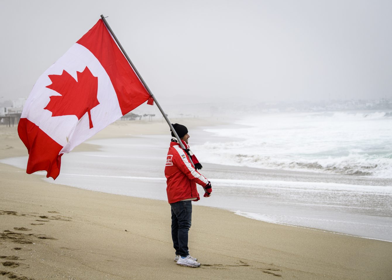 L'entraîneur de Mathea Olin avec le drapeau canadien lors de la finale de longboard féminin des Jeux panaméricains de Lima 2019, le 4 août 2019. Photo : Vincent Ethier/COC