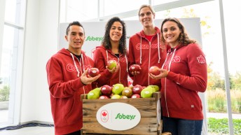 Quatre athlètes d'Équipe Canada sourient avec une pomme à la main.