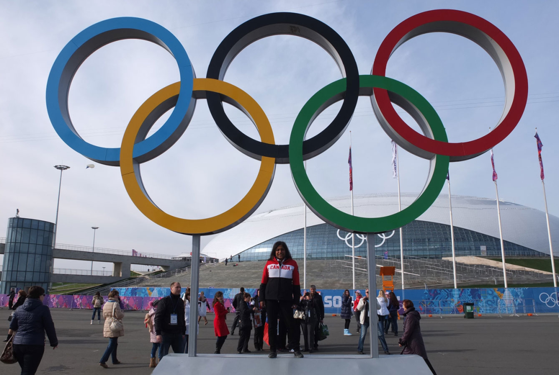 Shanti, une bénévole d'Équipe Canada, pose devant les anneaux olympiques dans le Parc olympique de Sotchi 2014.