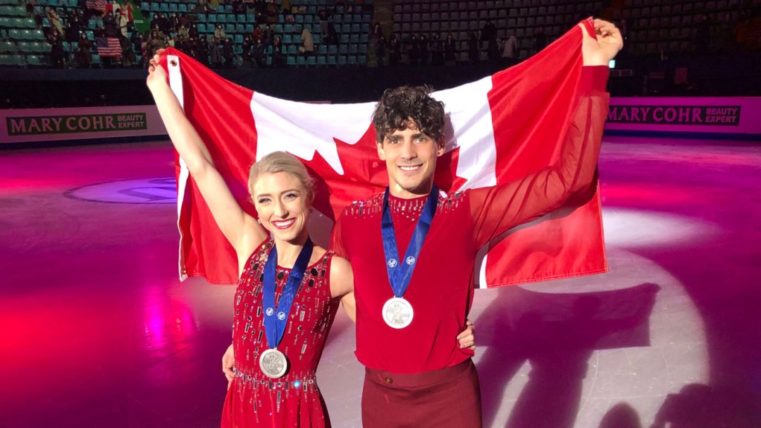 Deux patineurs posent avec le drapeau canadien et leurs médailles d'argent sur la patinoire
