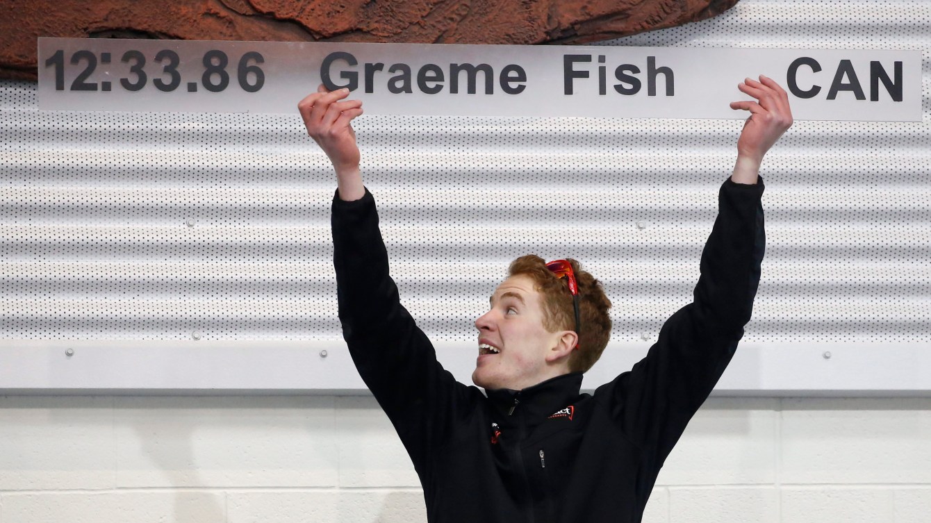 Graeme Fish les deux bras dans les airs pointe son record affiché au mur. 
