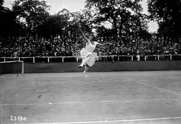 Équipe-canada-suzanne_lenglen_1922 Une joueuse de tennis des années 1920 dans une grande robe blanche saute pour atteindre la balle