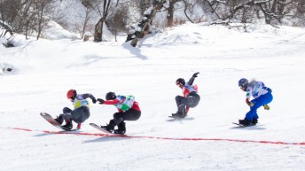 Quatre athlètes de snowboard cross s'apprêtent à franchir la ligne d'arrivée dans une finale très serrée.