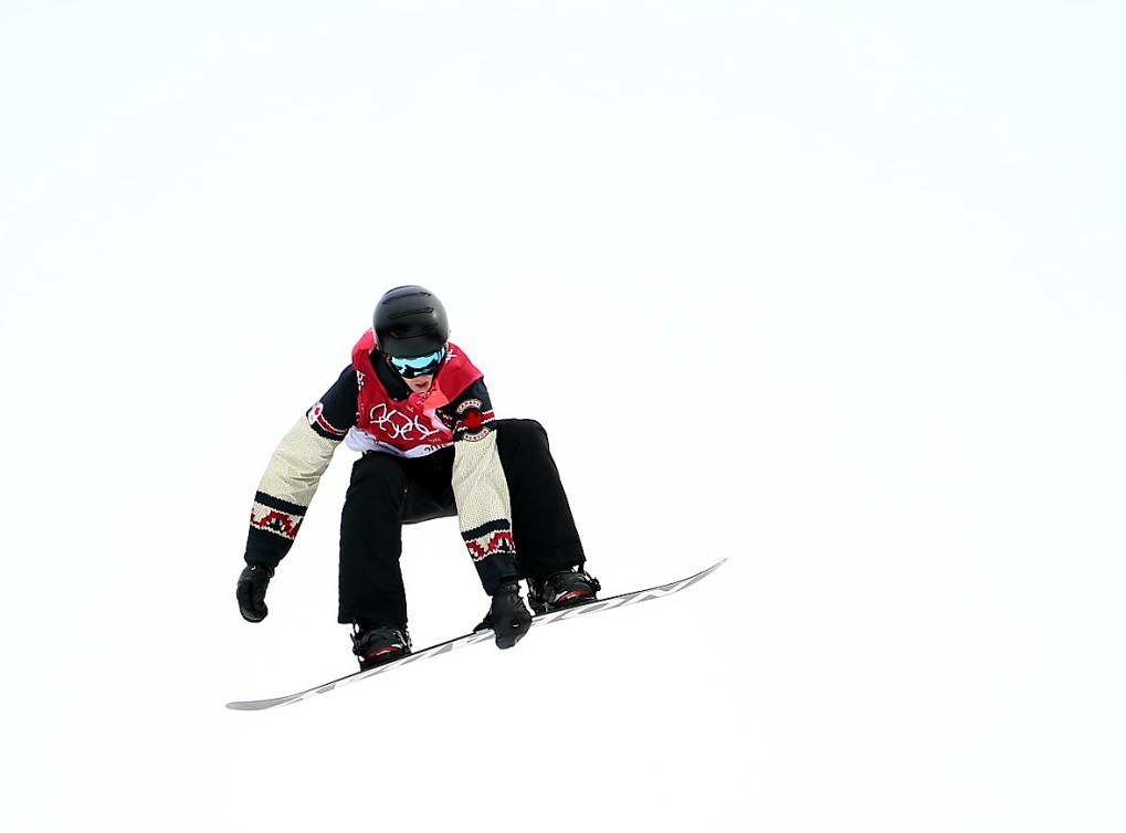 Un athlète de snowboard dans les airs touche sa planche d'une main.