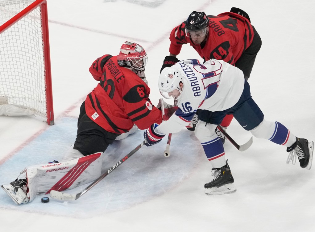 Le gardien de but d'Équipe Canada Eddie Pasquale fait un arrêt face à l'attaquant de l'équipe des États-Unis Nick Abruzzese alors que Mark Barberio d'Équipe Canada se déplace lors de l'action préliminaire de hockey sur glace masculin en première période aux Jeux olympiques d’hiver de Beijing 2022.