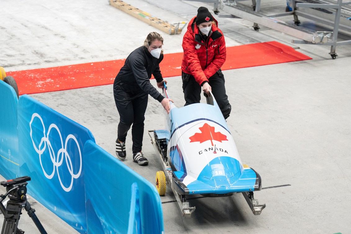 Deux femmes en survêtement poussent un bobsleigh.