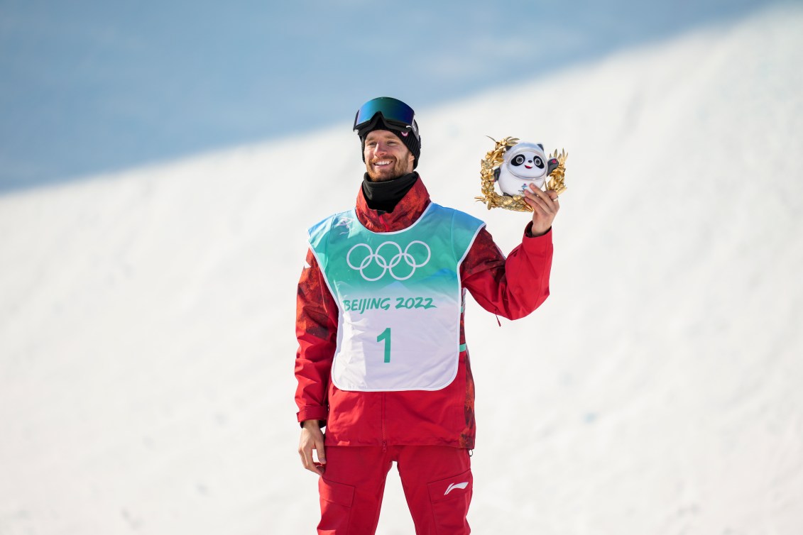 Le planchiste d'Équipe Canada Max Parrot sourit en tenant la mascotte des jeux sur le podium de big air en snowboard masculin à Beijing 2022.