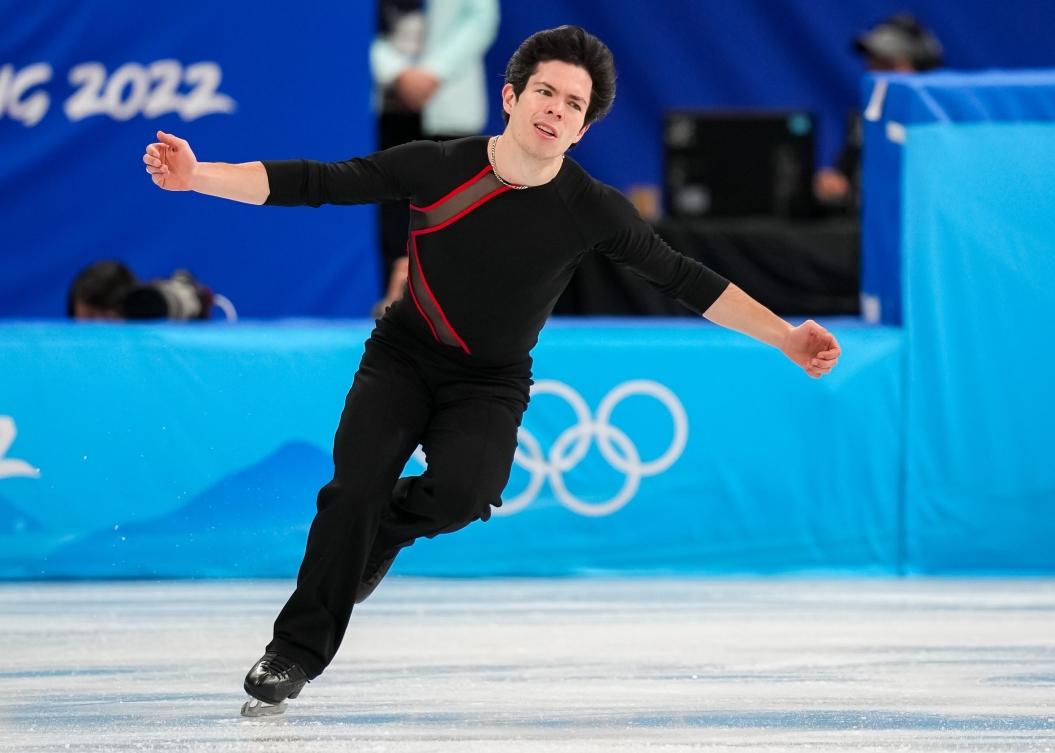 Keegan Meessing porte un pantalon noir et un chandail noir avec des lignes rouge. Il patine les bras en croix.