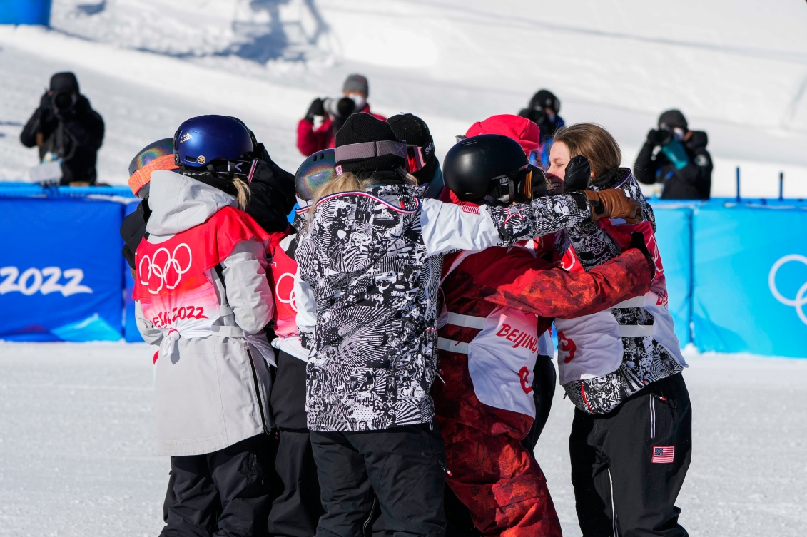 Équipe-Canada-Laurie-Blouin-snowboard-Beijing-2022 La planchiste d'Équipe Canada Laurie Blouin serre un groupe de compétitrices dans ses bras après avoir participé à l'épreuve féminine de snowboard.