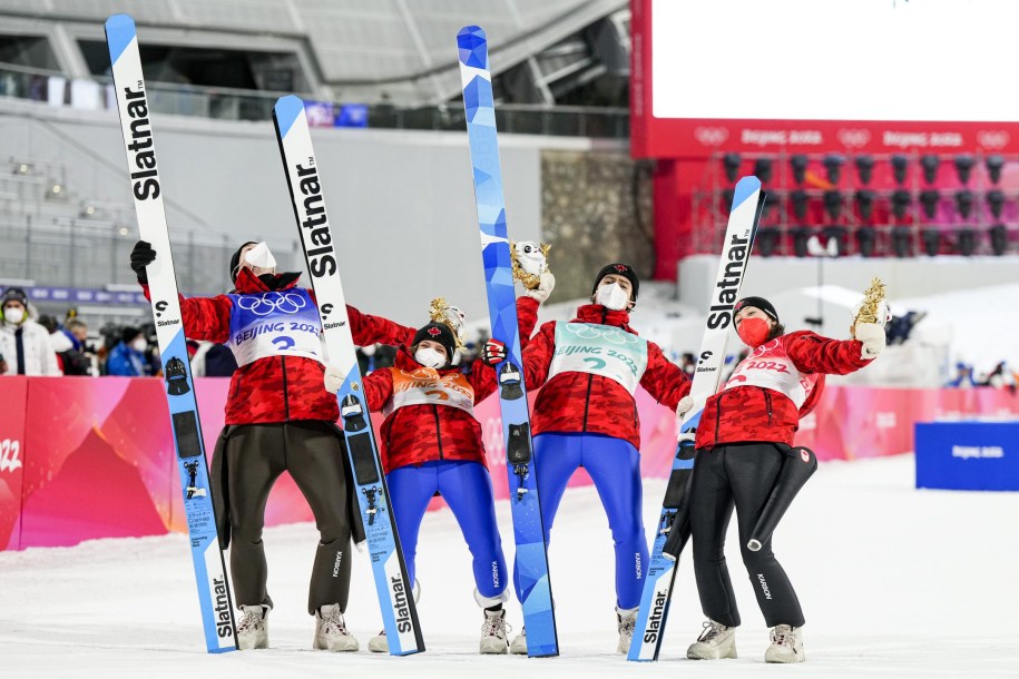 Les quatre skieurs de l'équipe mixte de saut à ski se tiennent par les épaules en basculant vers l'arrière.