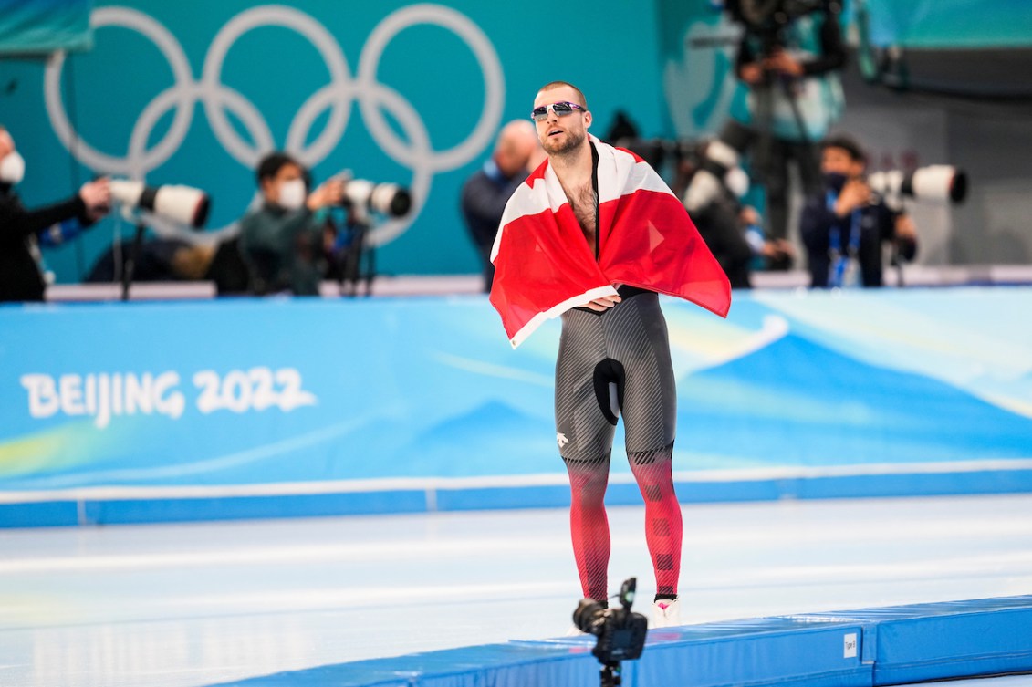 Laurent Dubreuil, épuisé, patine fièrement sur la glace, entourant ses épaules du drapeau Canadien, après sa course en patinage de vitesse sur longue piste au 1000 mètres, qui lui a valu la médaille d'argent. 