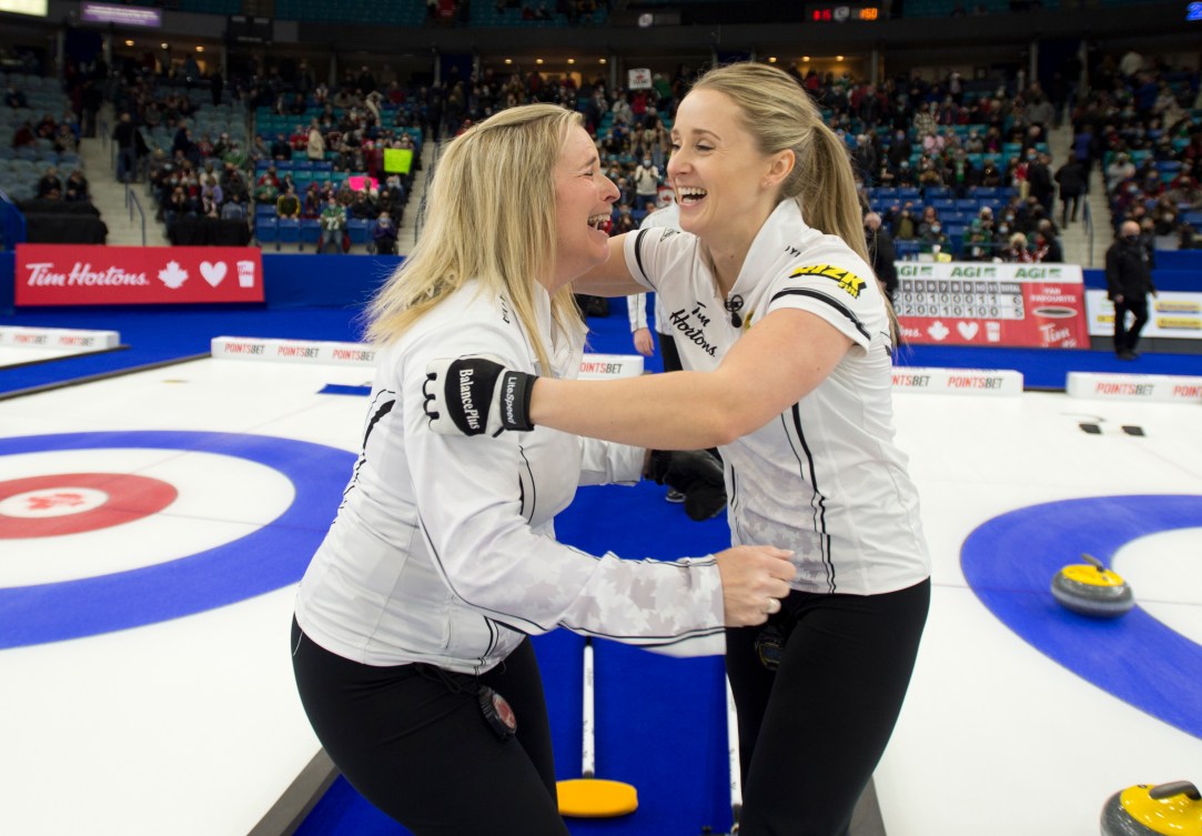 Deux joueuses de curling s'enlacent heureuses et souriantes.