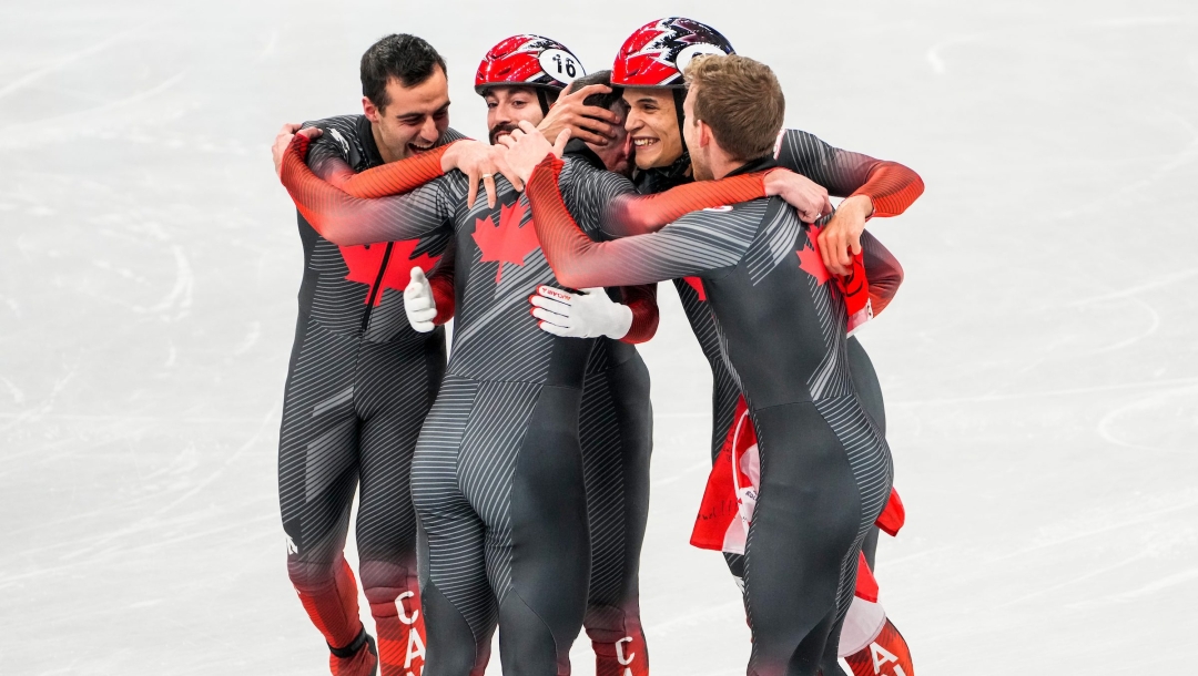Les patineurs de vitesse sur courte piste d'Équipe Canada s'entrelacent sur la glace pour célébrer leur médaille d'or gagnée au relais de 5000 mètres à Beijing 2022
