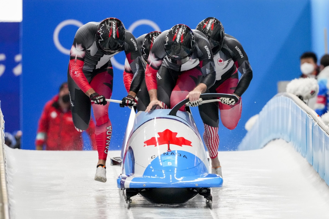 Quatre bobeurs courent en poussant leur traîneau en début de course.