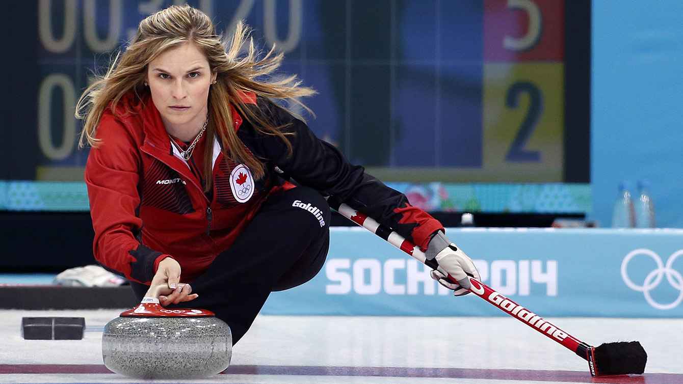 La capitaine canadienne Jennifer Jones regarde droit devant, s'appuie sur son balais et s'apprête à lancer une pierre aux Jeux de Sotchi 2014.