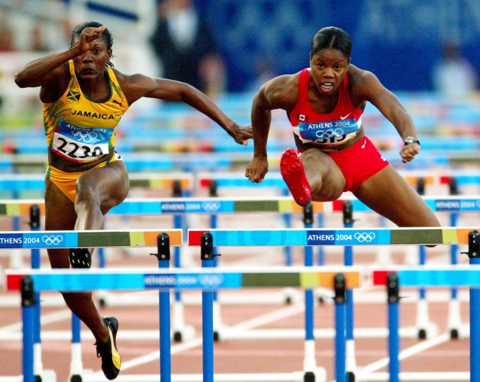 Perdita Felicien élance une jambe vers l'avant alors qu'elle saute à toute vitesse un obstacle à l'épreuve du 100 mètres haies féminin en athlétisme à Athènes 2004.