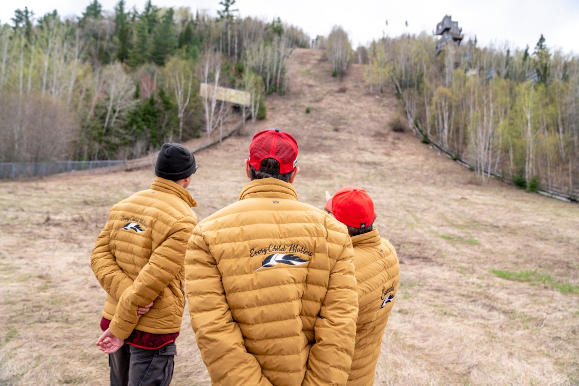 Trois hommes regardent une pente. On les voit de dos.