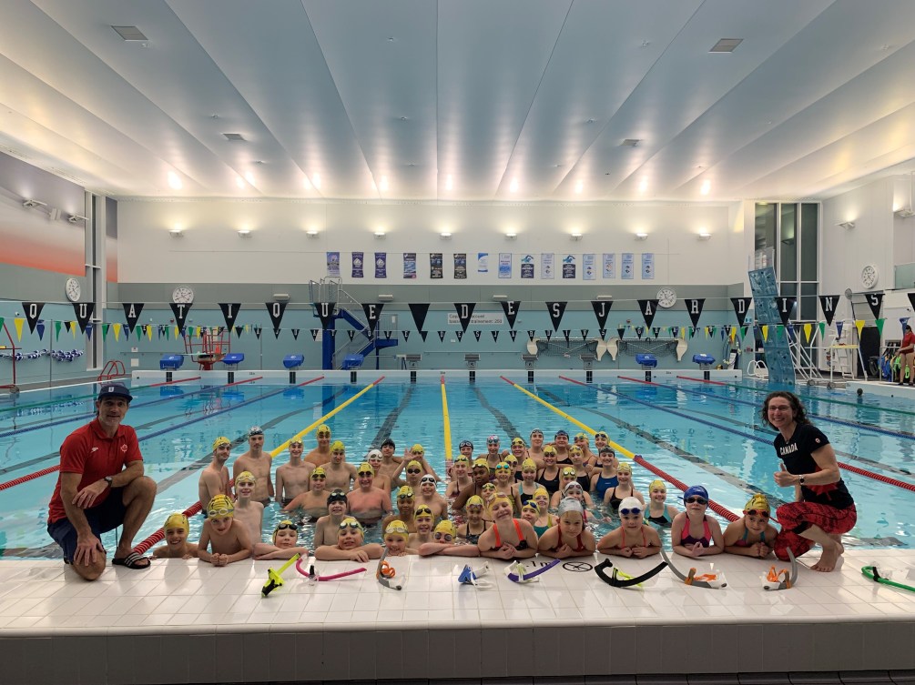 Des jeunes nageurs posent dans la piscine avec deux entraîneurs. 