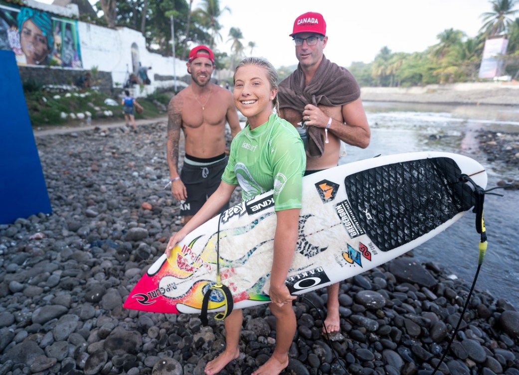 Erin Brooks tient sa planche de surf tout en souriant à la caméra avec ses coéquipiers