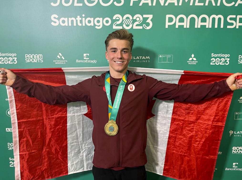 Félix Dolci arbore le drapeau canadien derrière lui, médaille d'or au cou.