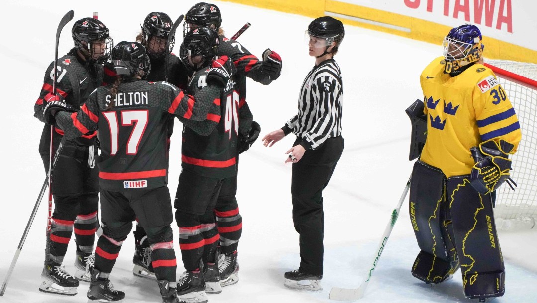 Cinq joueuses canadiennes rassemblées en cercle sur la glace.