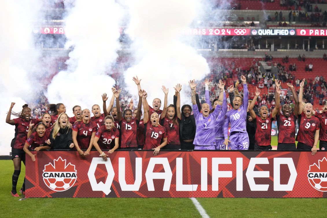 L'équipe canadienne féminine de soccer célèbre derrière une bannière indiquant qu'elle est qualifiée