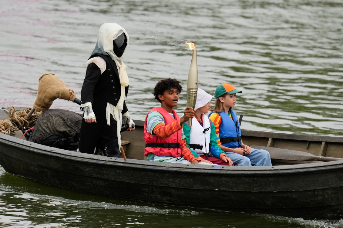 La flamme olympique est portée par des enfants et une figure masquée dans un bateau. 