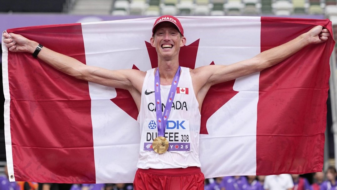 Evan Dunfee tient le drapeau canadien derrière lui, une médaille d’or autour du cou sur son maillot blanc