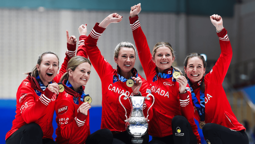 Cinq joueuses de curling vêtues de vestes rouges célèbrent avec un trophée tout en portant des médailles d’or.