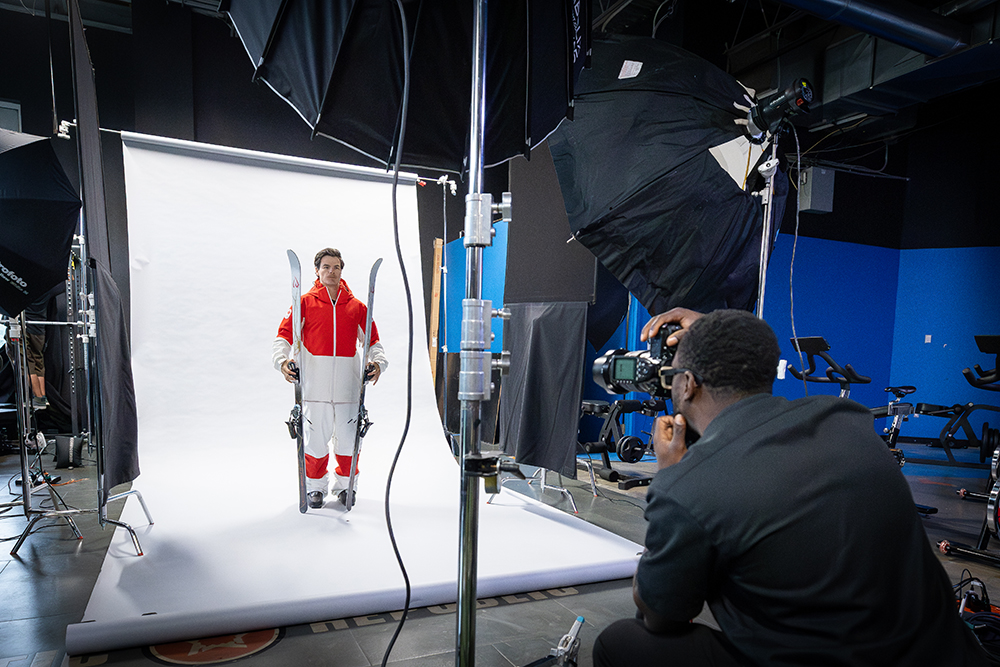 Mikaël Kingsbury, vêtu d'une tenue de ski blanche et rouge sur fond blanc, tient ses skis verticalement de chaque côté de son corps et regarde l'objectif.