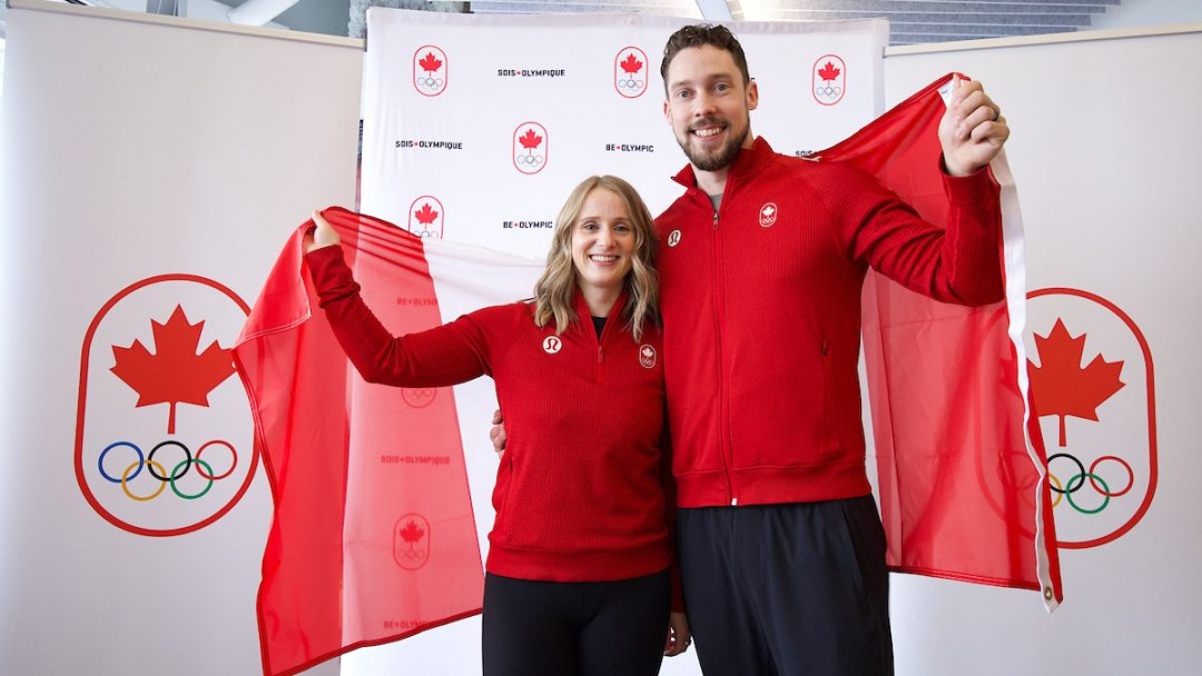 Vêtus de hauts rouges et de pantalons noirs, Jocelyn Peterman et Brett Gallant tiennent un drapeau canadien derrière eux.