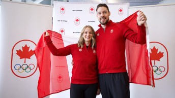 Vêtus de hauts rouges et de pantalons noirs, Jocelyn Peterman et Brett Gallant tiennent un drapeau canadien derrière eux.