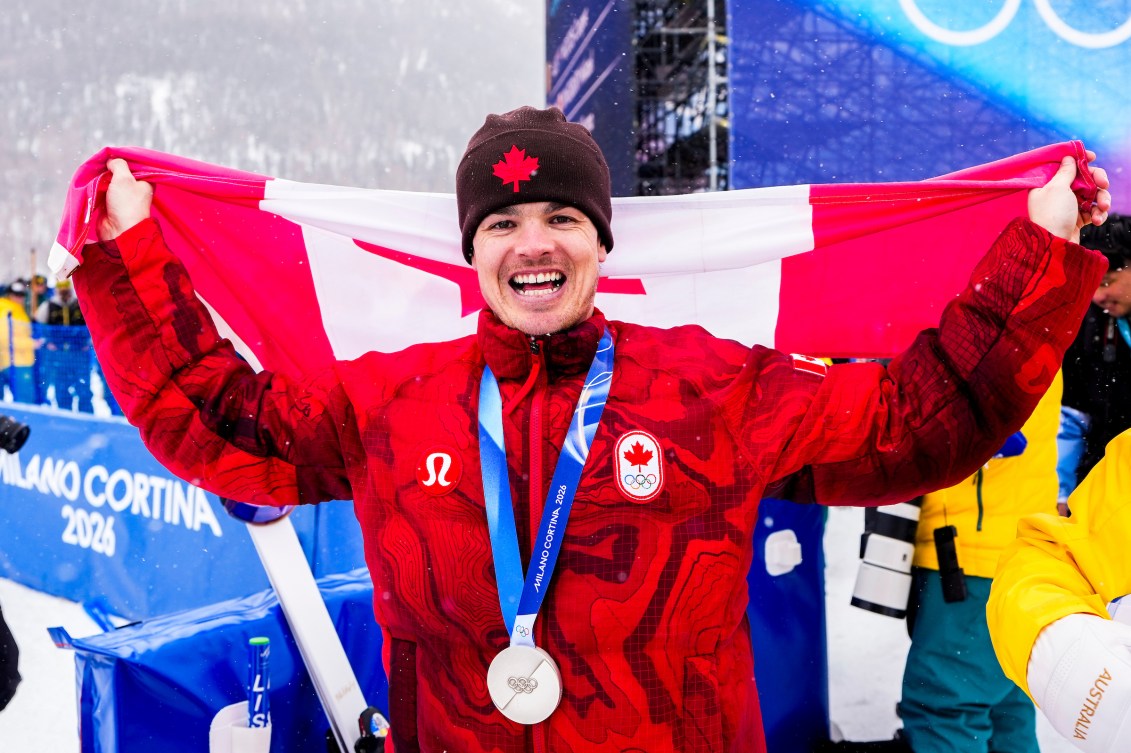 Mikaël Kingsbury tient le drapeau canadien derrière lui.