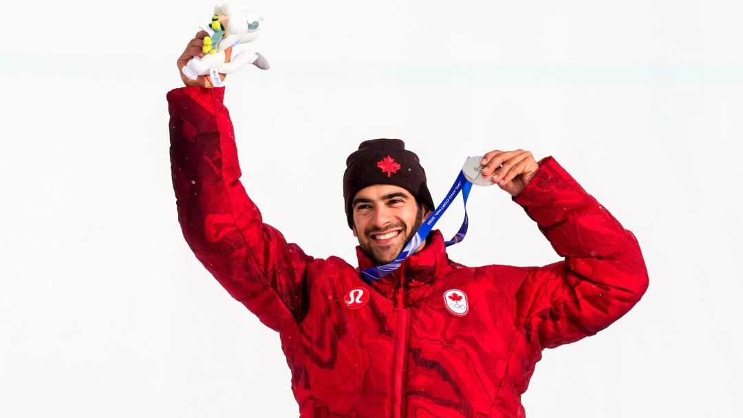 Éliot Grondin, tout sourire, célèbre sa médaille d'argent en la tenant dans ses mains, avec le toutou mascotte des olympiques dans l'autre main.