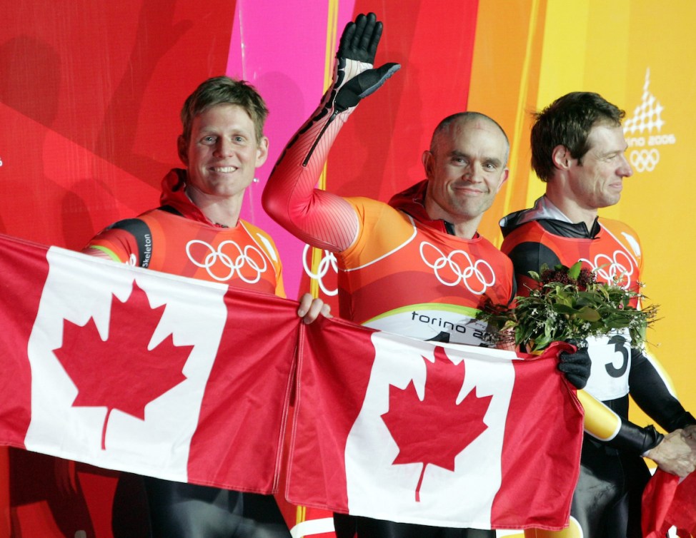 Duff Gibson and Jeff Pain hold Canadian flags in front of them in the finish area after a skeleton race