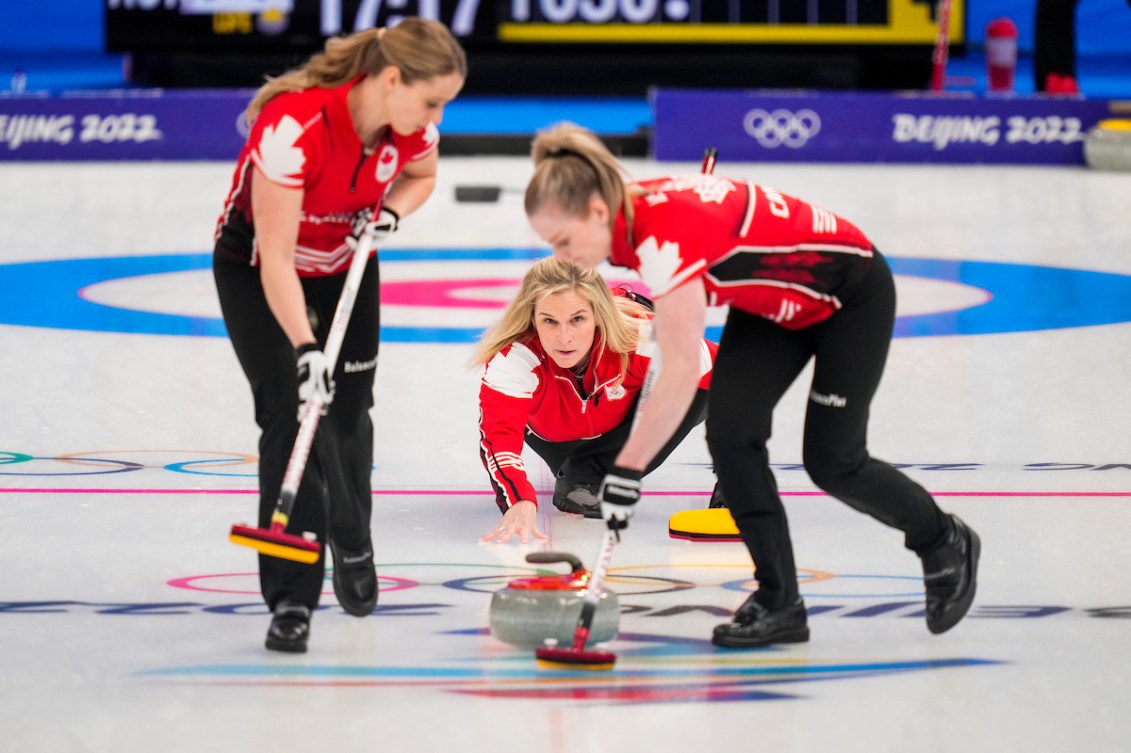 Female curler in red throws a red stone for her teammates to sweep 