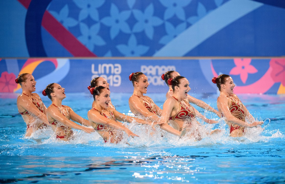 Eight artistic swimmers perform arm movements above the water