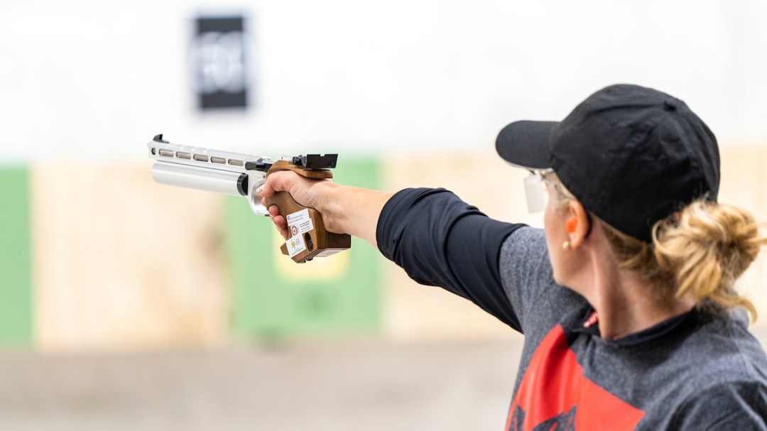 A woman fires an air pistol at a target in competition