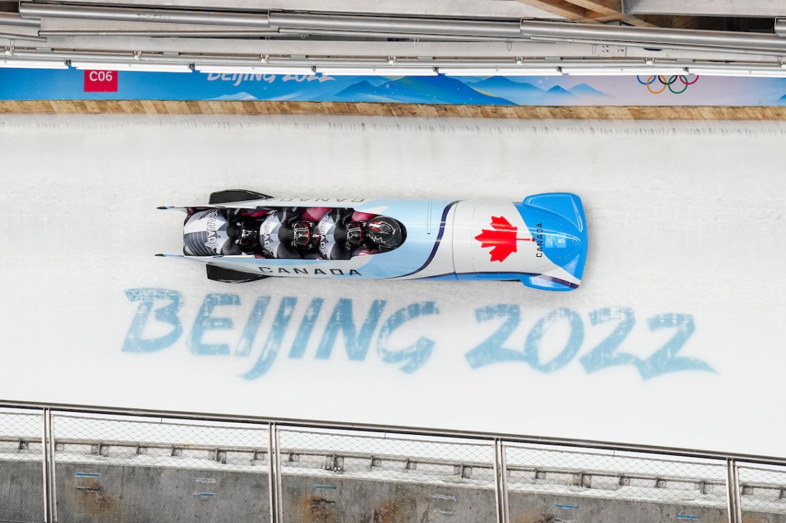 A blue Canadian four man bobsled as viewed from overhead goes over the Beijing 2022 logo on the ice track 