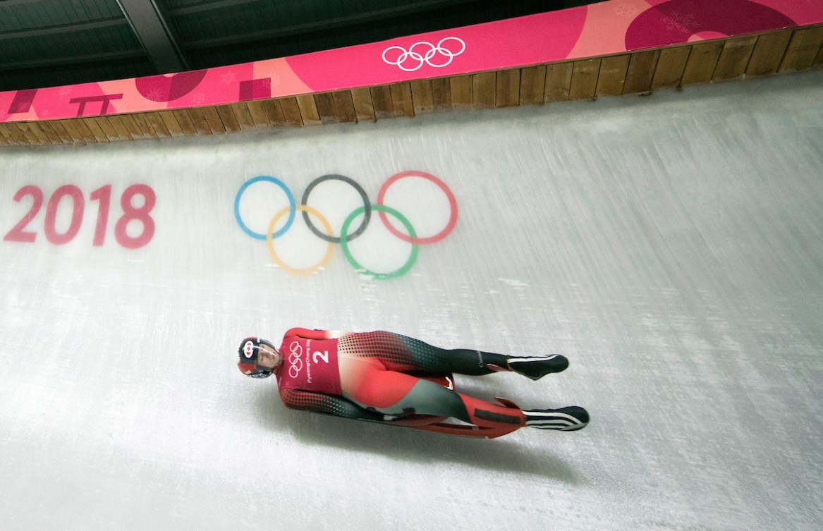 Luger in a black and red suit slides past the Olympic rings