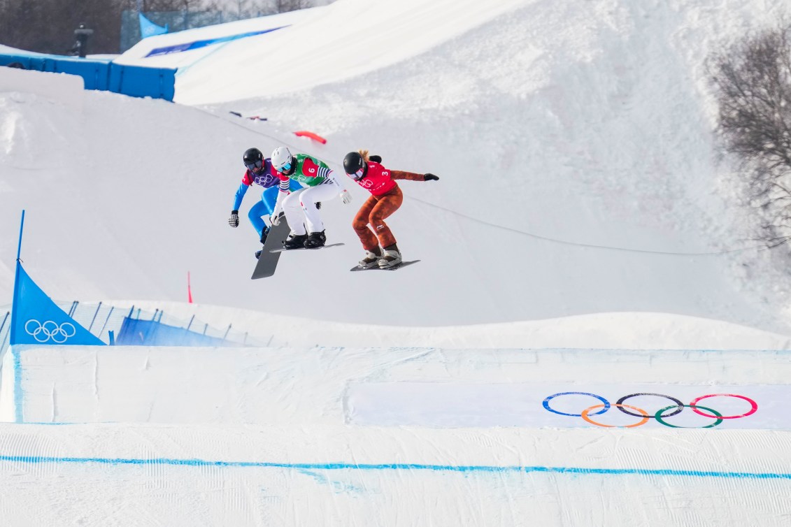 Three snowboarders fly through the air across on a snowboard cross course