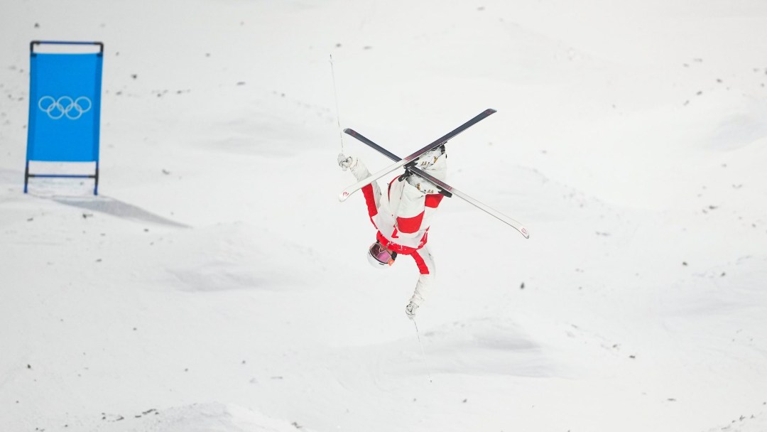 Mikael Kingsbury performs an upside down aerial trick with his skis crossed on a moguls course