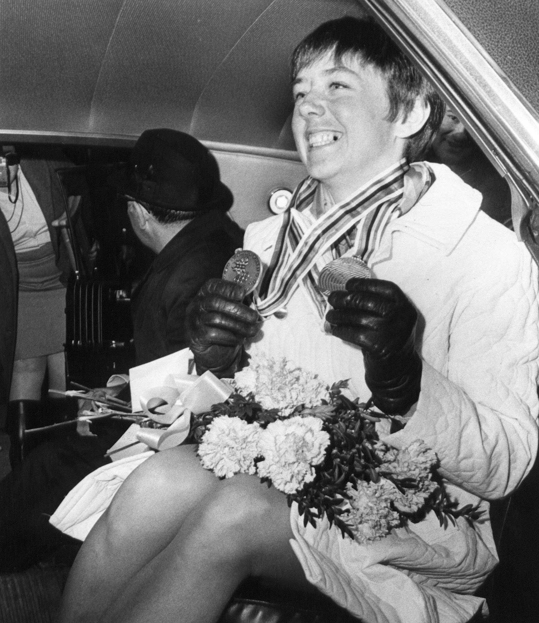 Black and white photo of Nancy Greene sitting in a car wearing medals