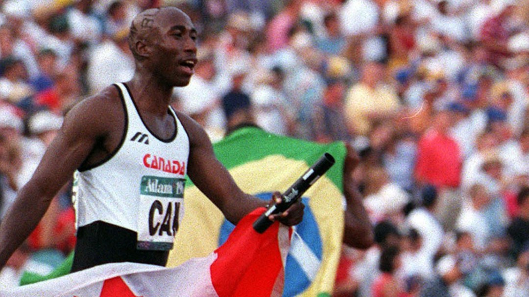 Robert Esmie holds onto the relay baton and Canadian flag after winning the race.