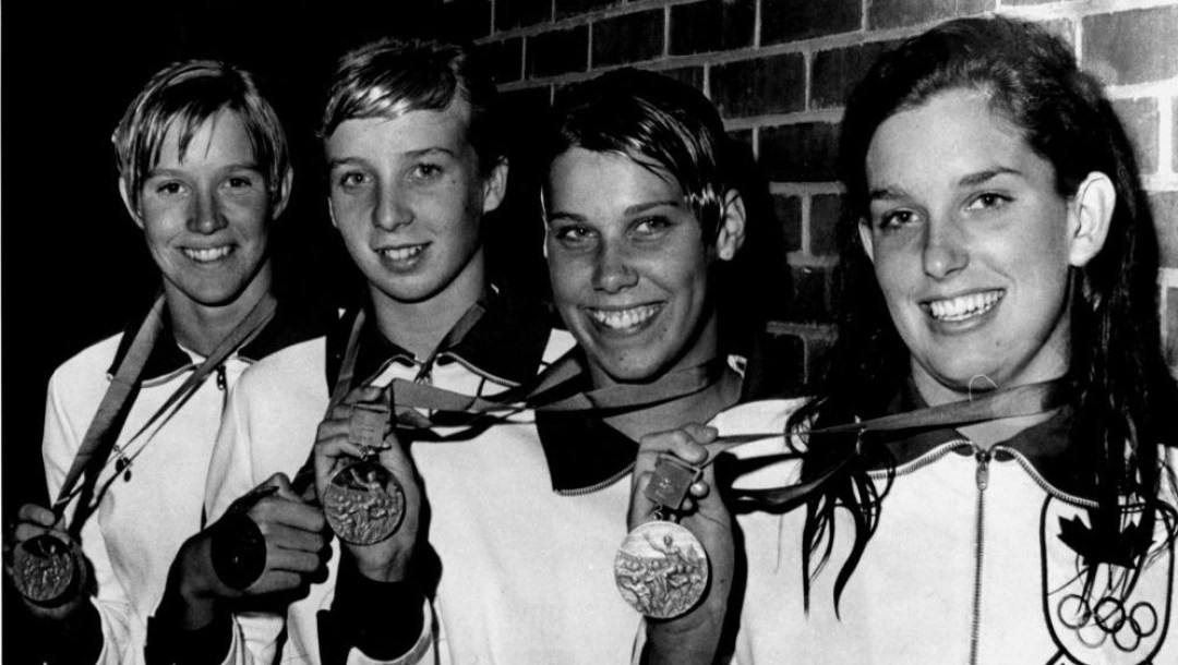 A black and white photo of four female swimmers holding up Olympic medals.